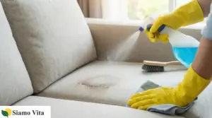 Persona con guanti gialli spruzza detergente su un divano in tessuto macchiato e lo pulisce con un panno